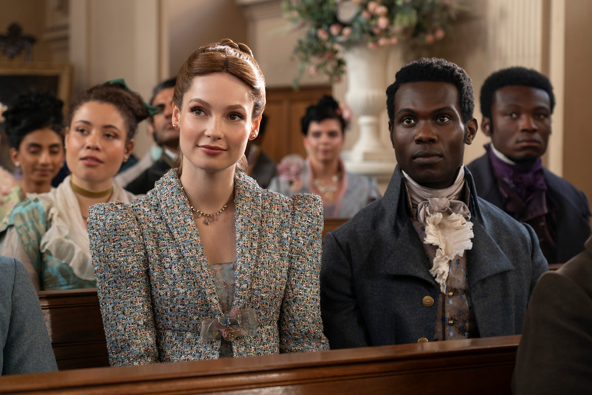 Victor Alli as John Stirling and Hannah Dodd as Francesca Bridgerton stand in a sitting room together smiling in Season 3 of ‘Bridgerton’