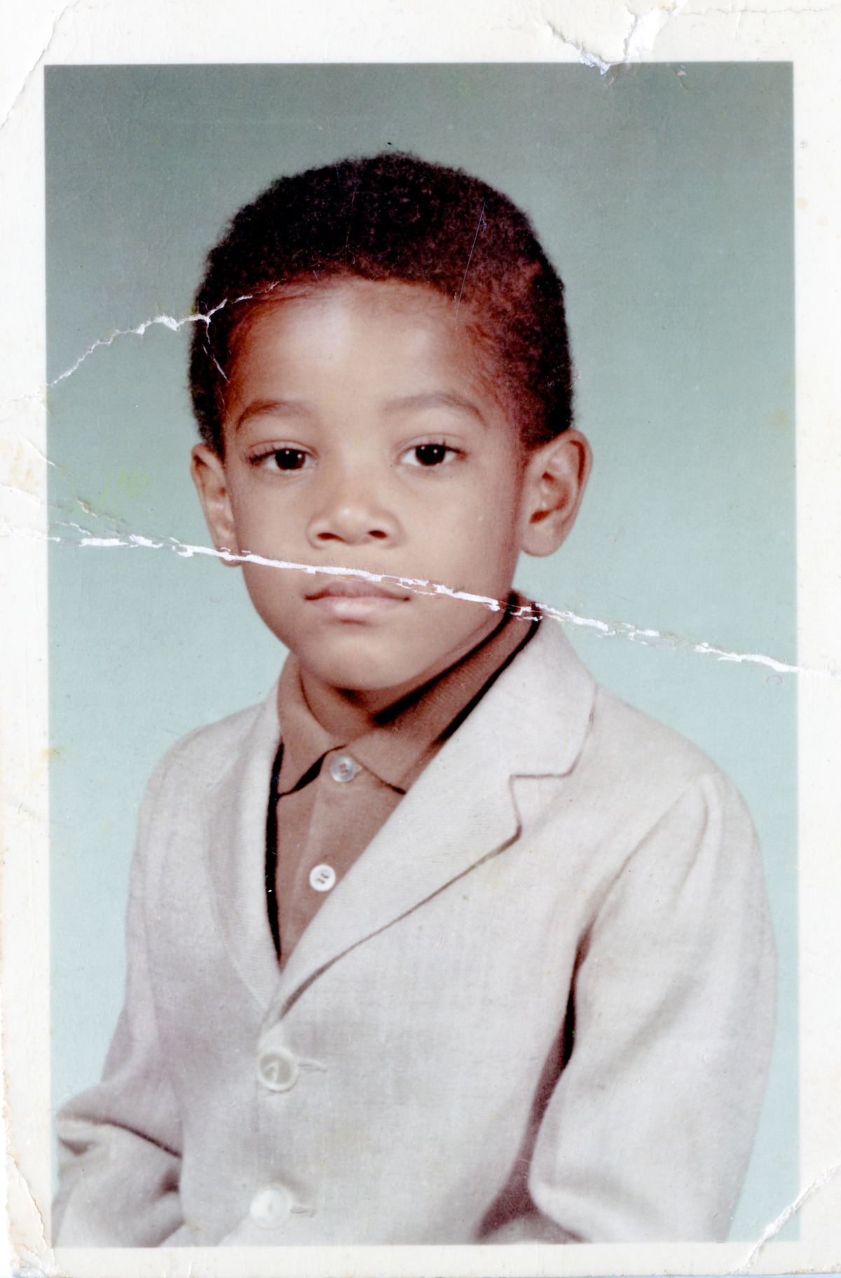 A folded, faded picture of a portrait of a young Black boy in a linen suit and collared shirt.