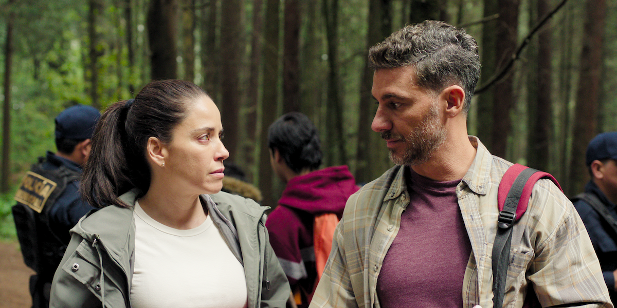 Ana Claudia Talancón as Daniela and Erick Elías as Fabián look at one another while standing in a forest in front of a group of people in an image from the series ‘The Accident.’