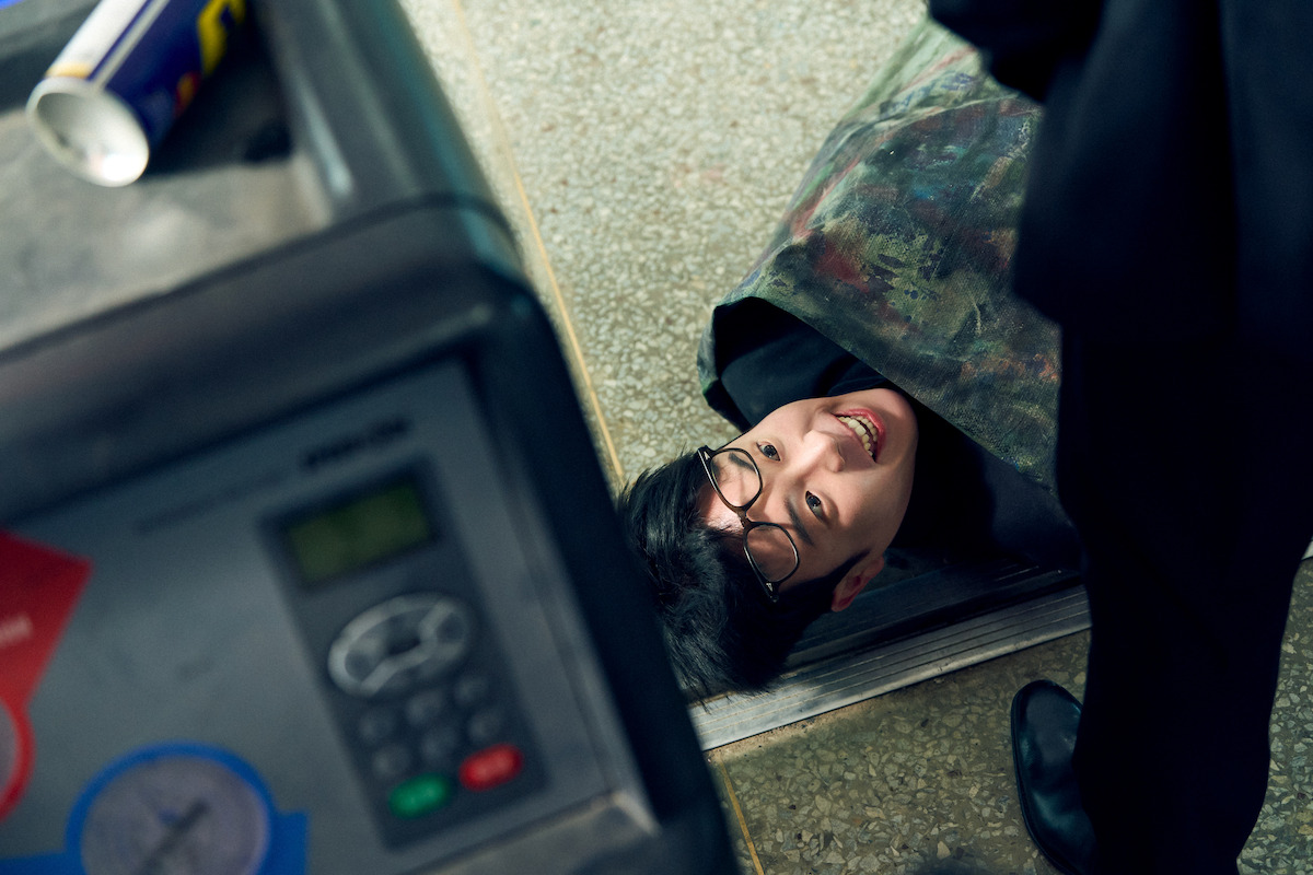 A handsome gentleman lies on the ground with a menacing smile as someone stands over him.