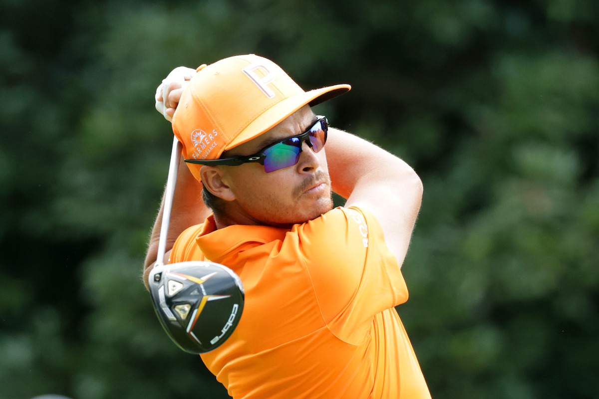 Golfer Rickie Fowler in head-to-toe orange holds still at the end of a long drive.