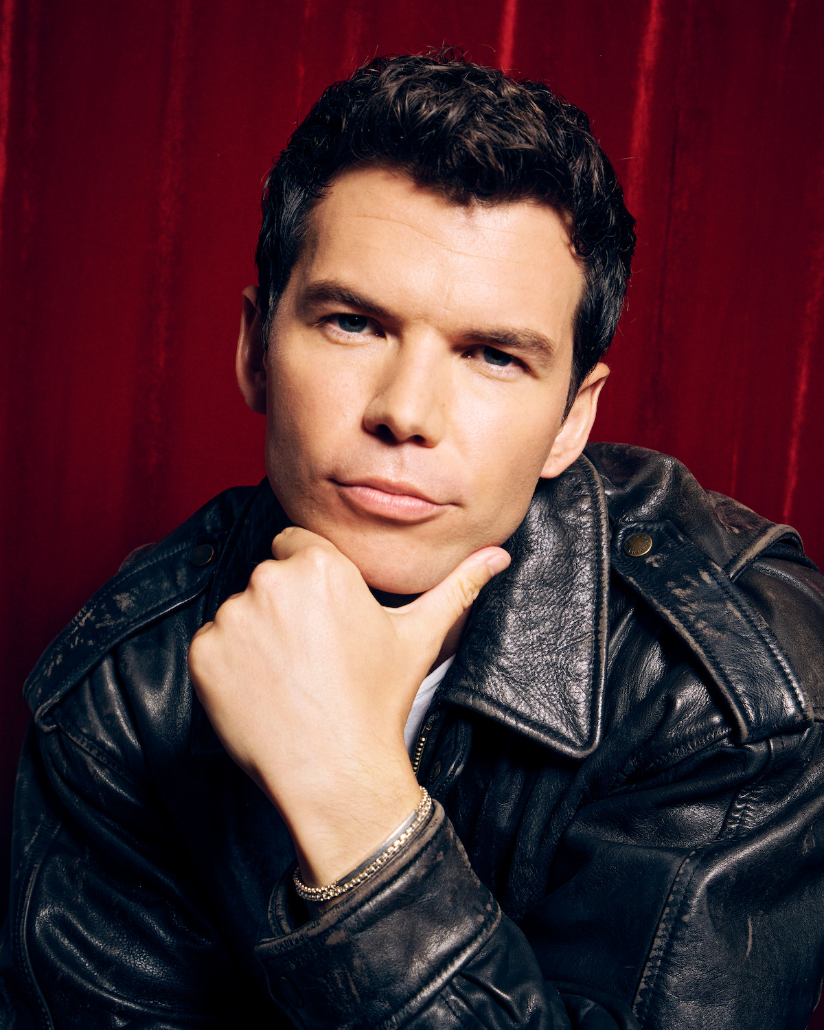 Luke Newton against a red photo booth backdrop