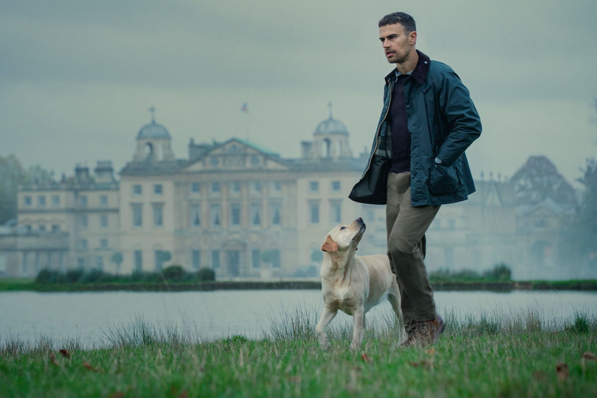 Theo James as Eddie Horniman walks near a body of water with a large estate in the background in Season 1 of ‘The Gentlemen’