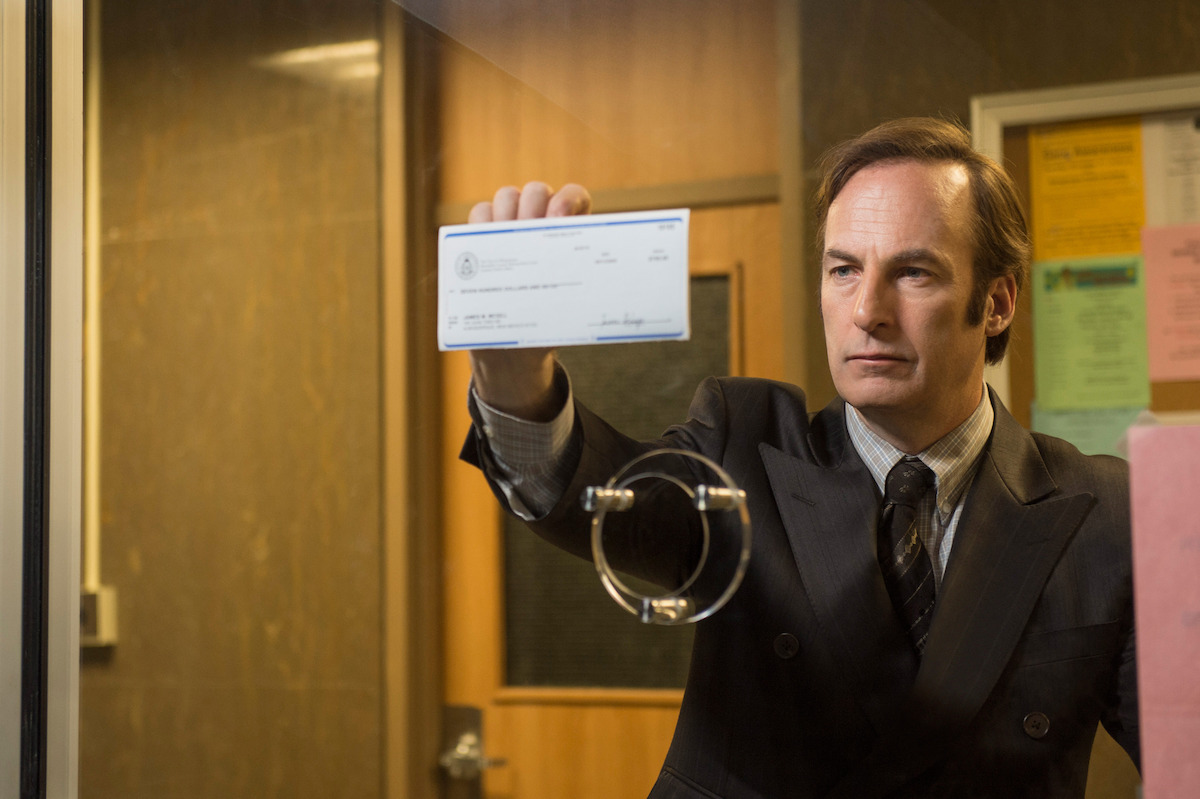 Saul Goodman holds up a check against a clerk's window. 