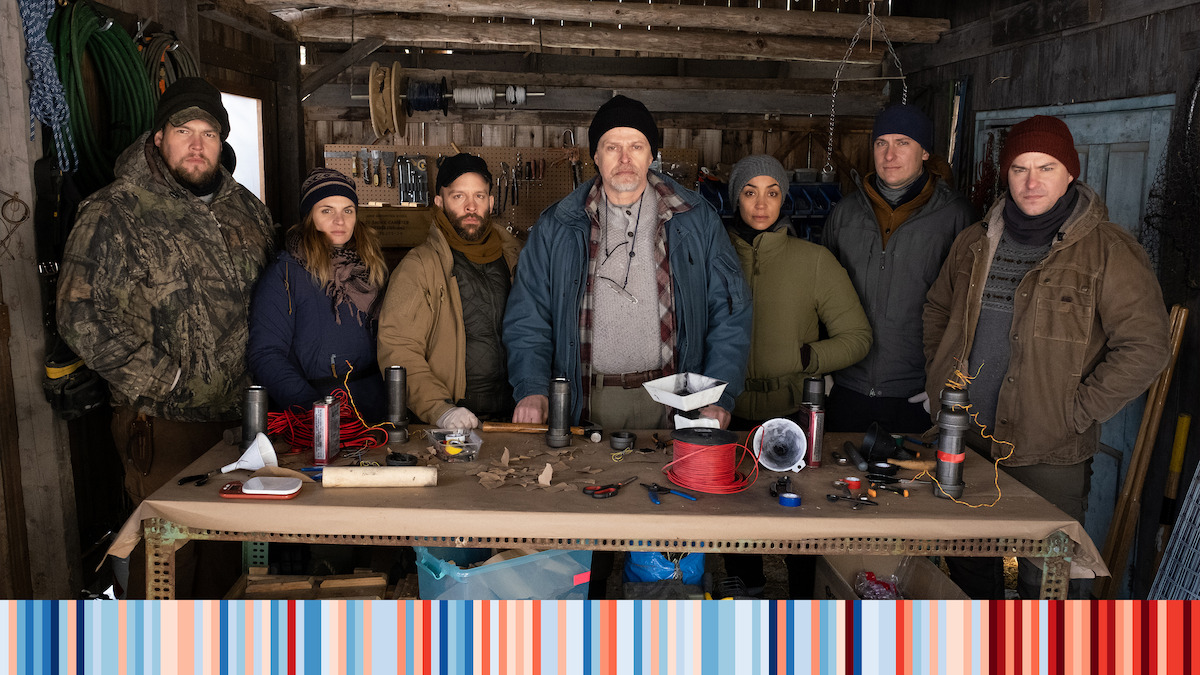 The Decline cast standing behind a table with electronics and other doodads 