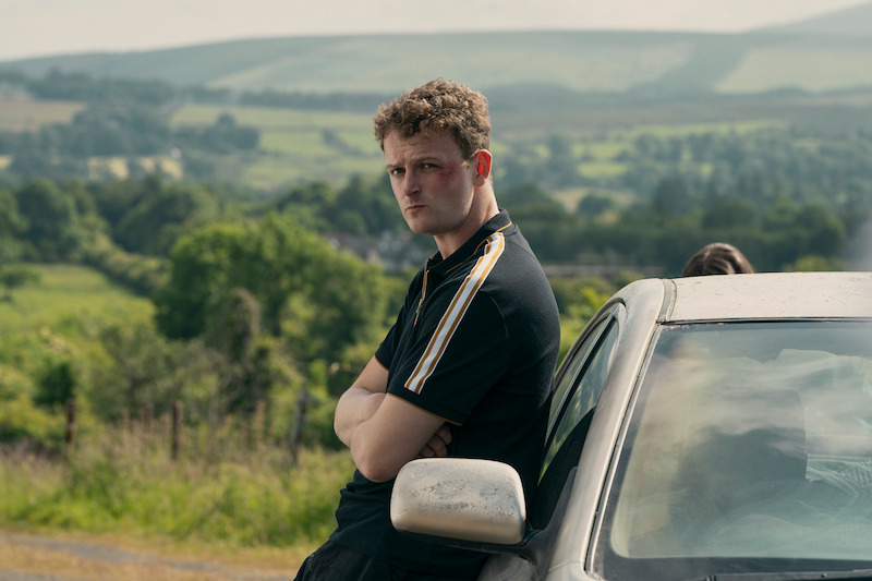 Chris Walley as Sean leans on a car in 'Bodkin'