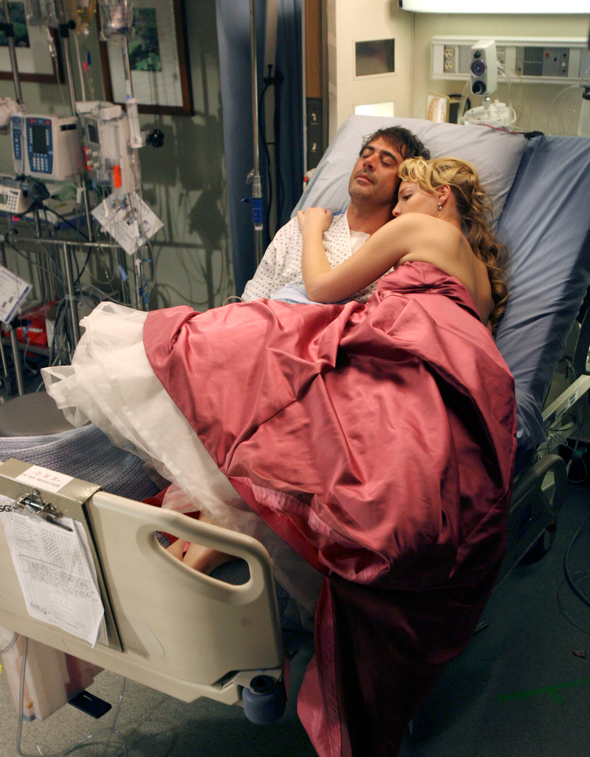 A woman wearing a fancy dress, lies next to a man in a hospital bed. 