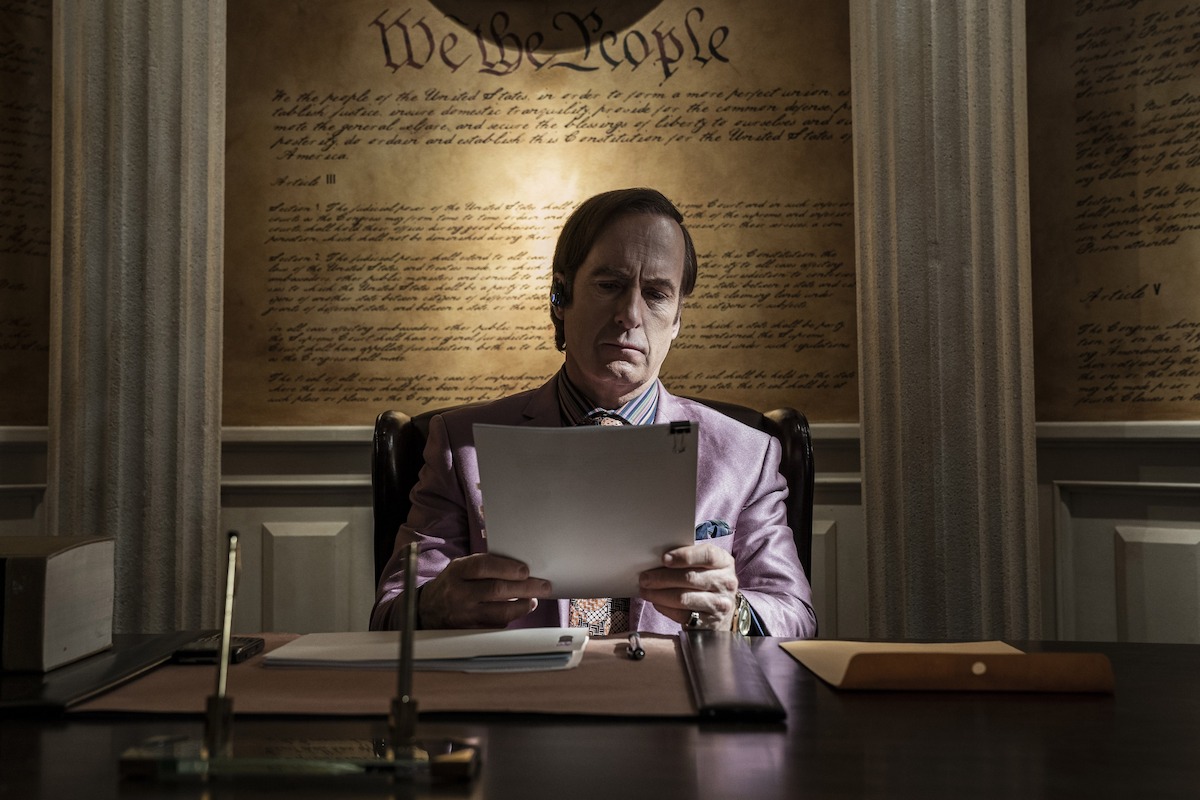 Saul Goodman in his law office with a mural of the constitution behind him. 