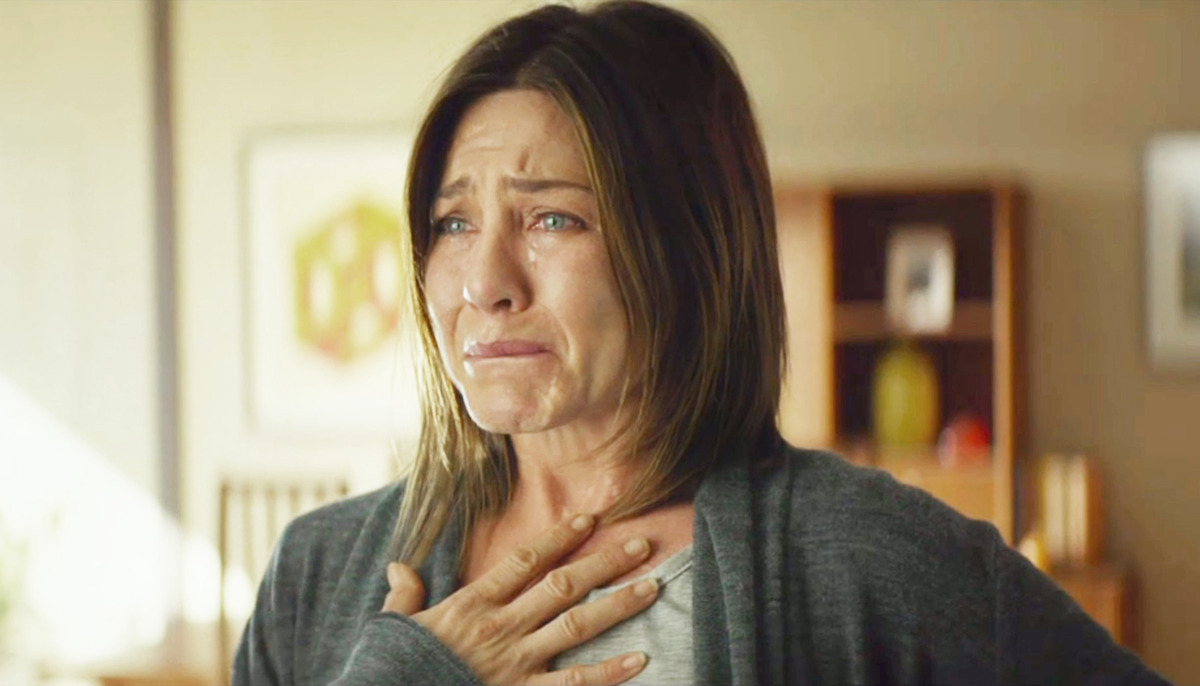 Aniston is crying holding a hand on her chest. 