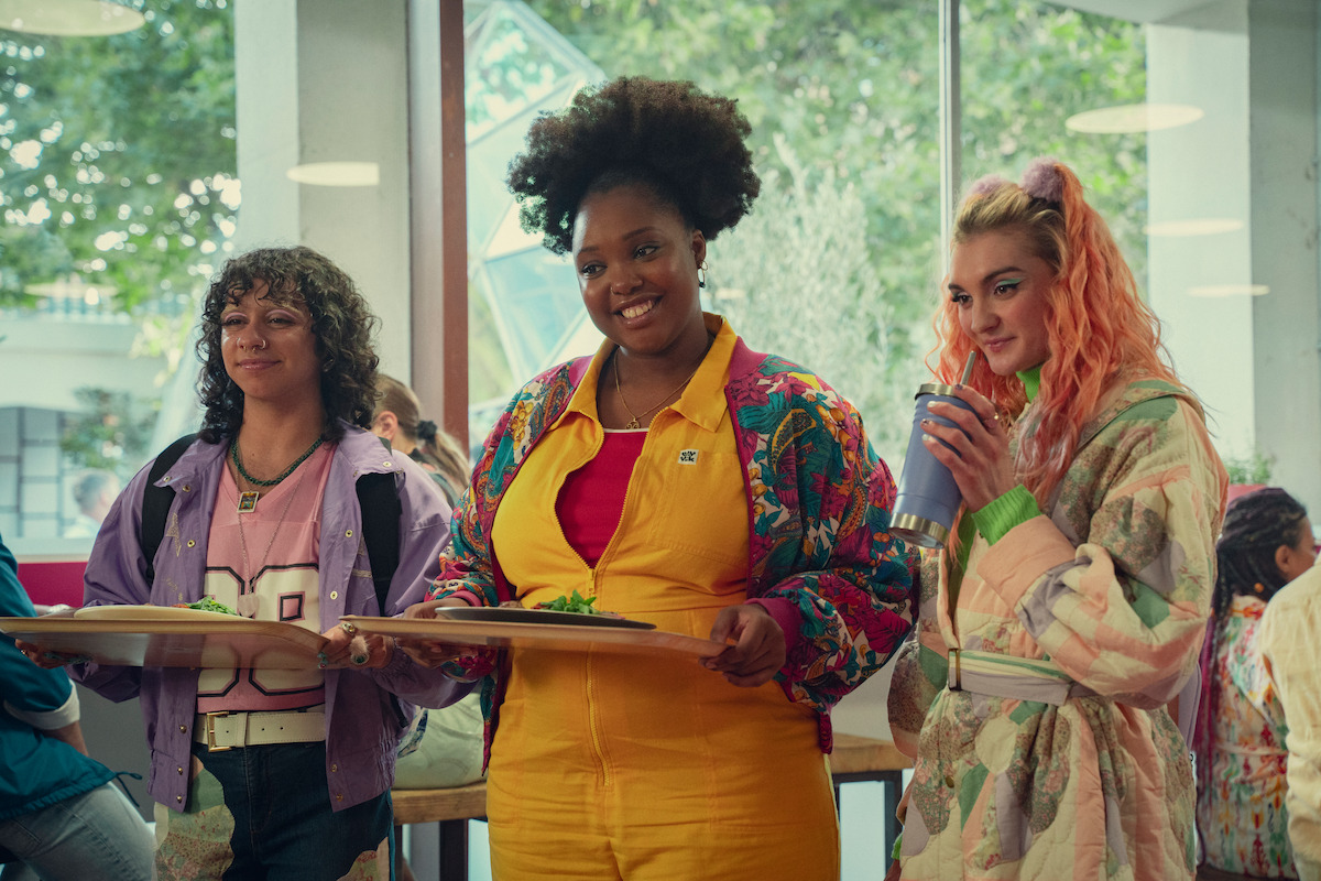 Felix Mufti as Roman, Alexandra James as Aisha, and Anthony Lexa as Abbi stand together smiling at school in Season 4 of 'Sex Education.'