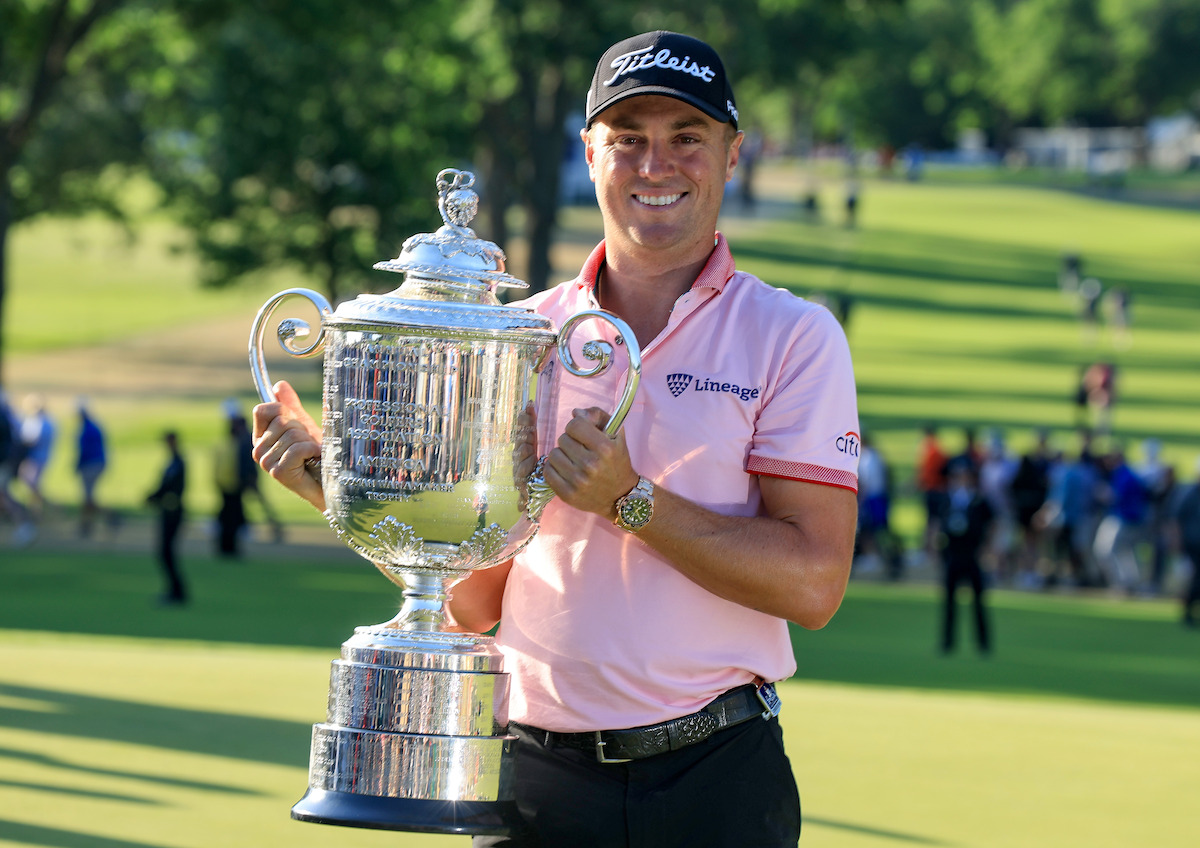 Golfer Justin Thomas holding a large silver trophy.
