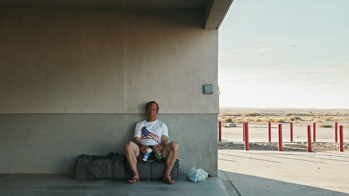 A sunburnt Saul Goodman rests at a gas station with a bottle of water. 