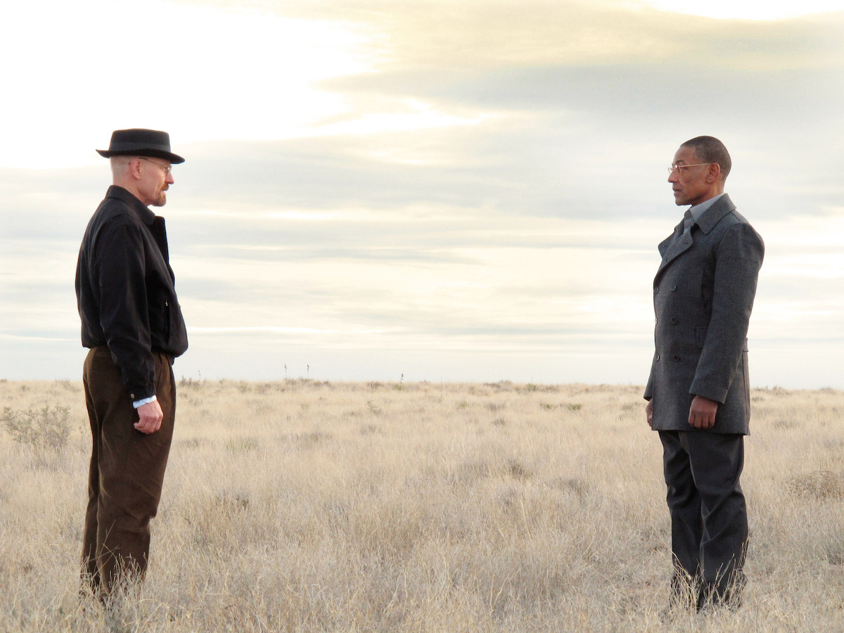 Walter White and Gus Fring stand opposite one another in the desert. 