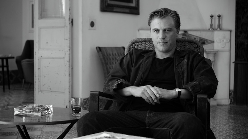 Johnny Flynn as Dickie Greenleaf sits in an armchair in 'Ripley'