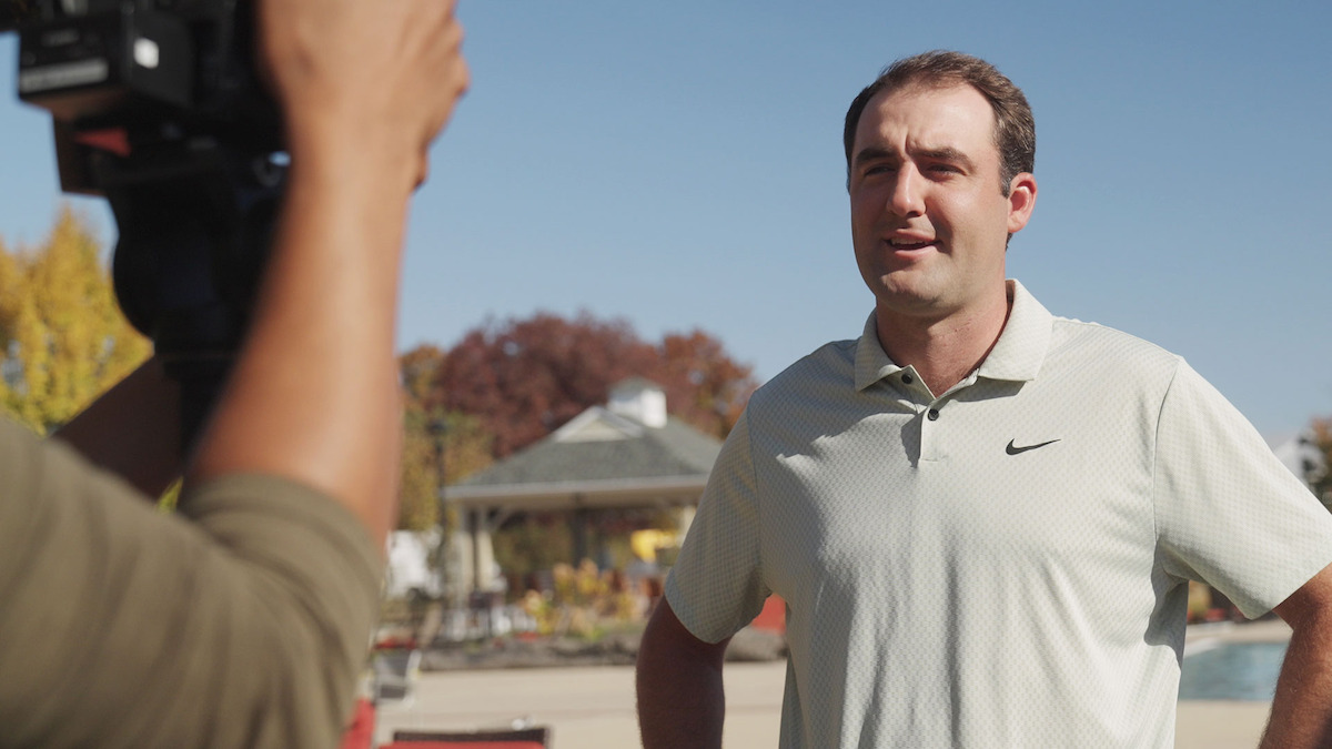 Scottie Scheffler being filmed in front of a camera wearing a white polo shirt.