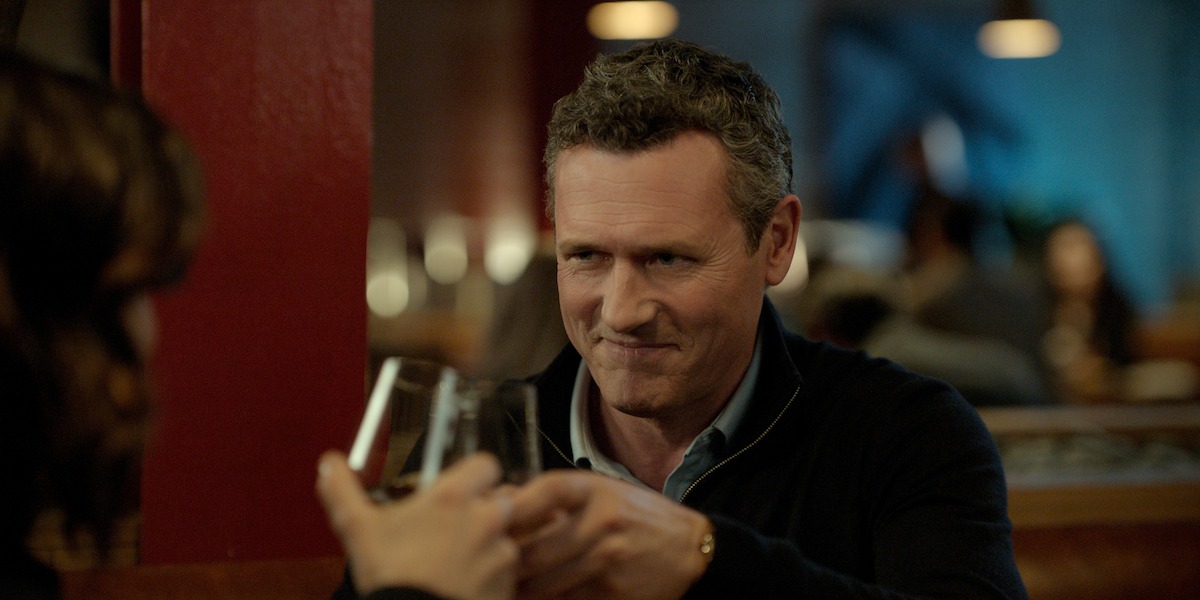 Man and woman clinking glasses at a restaurant table, warm lighting, other people blurred in the background, cozy and intimate dinner setting.