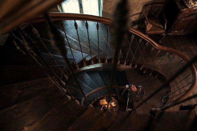 Lars Eidinger as Sergeant Major Reinhold von Rumpel screaming up at someone from the bottom of a spiral staircase. 