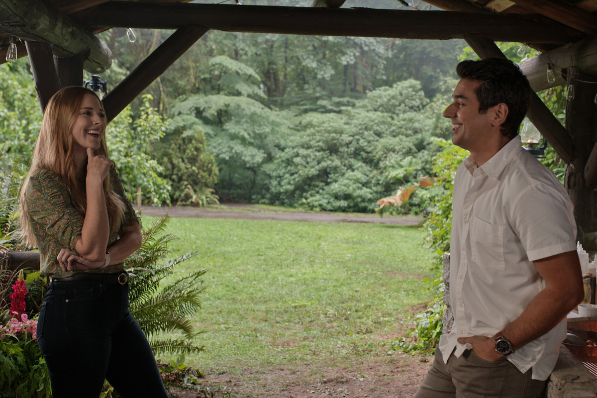 Alexandra Breckenridge as Mel Monroe and Mark Ghanimé as Dr. Cameron Hayek smile at each other on a porch in Season 4 of ‘Virgin River.’