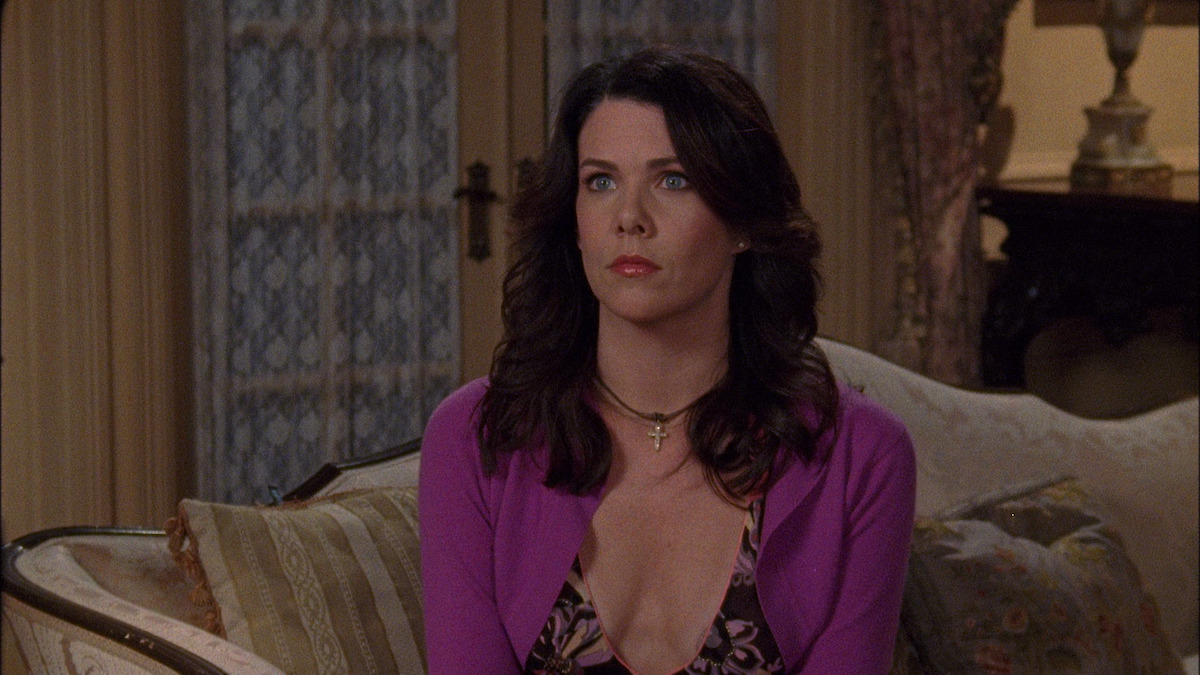 A woman in a black dress and purple cardigan sits on a sofa