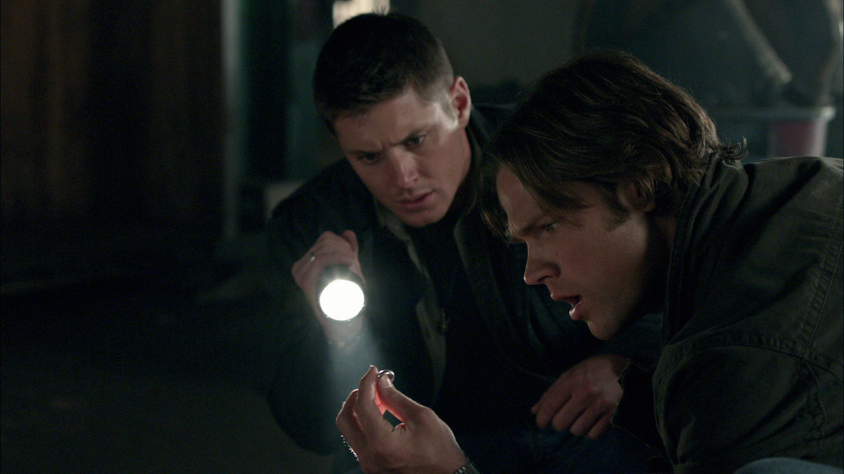 2 men looking at something off the ground, one man is using a flashlight to see