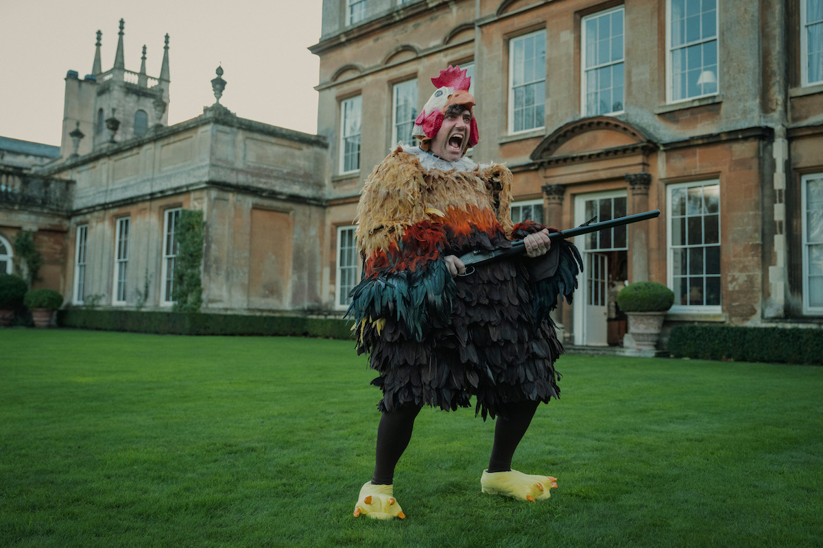 Daniel Ings as Freddy Horniman wears a chicken costume and holds a shotgun in Season 1 of ‘The Gentlemen’
