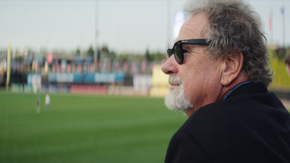 Mike Veeck wears sunglasses and looks out on a baseball field.