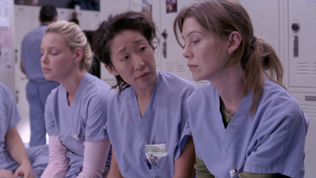 two doctors wearing scrubs talking to each other in a hospital locker room. 
