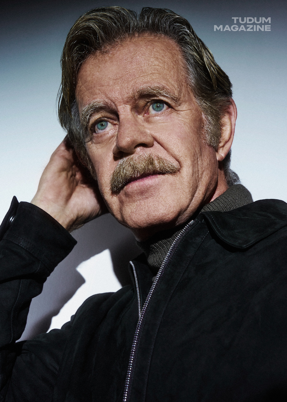 William H. Macy in a green turtleneck against a white background.