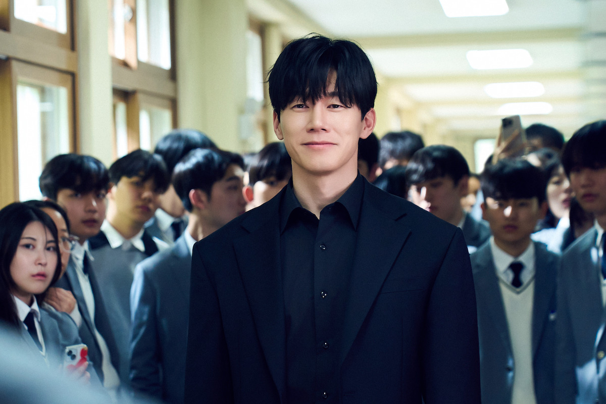 A gentleman in an all-black suit smiles with ease while a group of students look at him with anticipation.