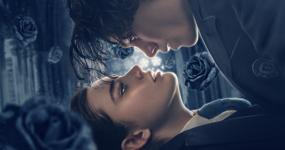 Caterina Ferioli as Nica and Simone Baldasseroni as Rigel look into each other's eyes with black roses falling around them in 'The Tearsmith'