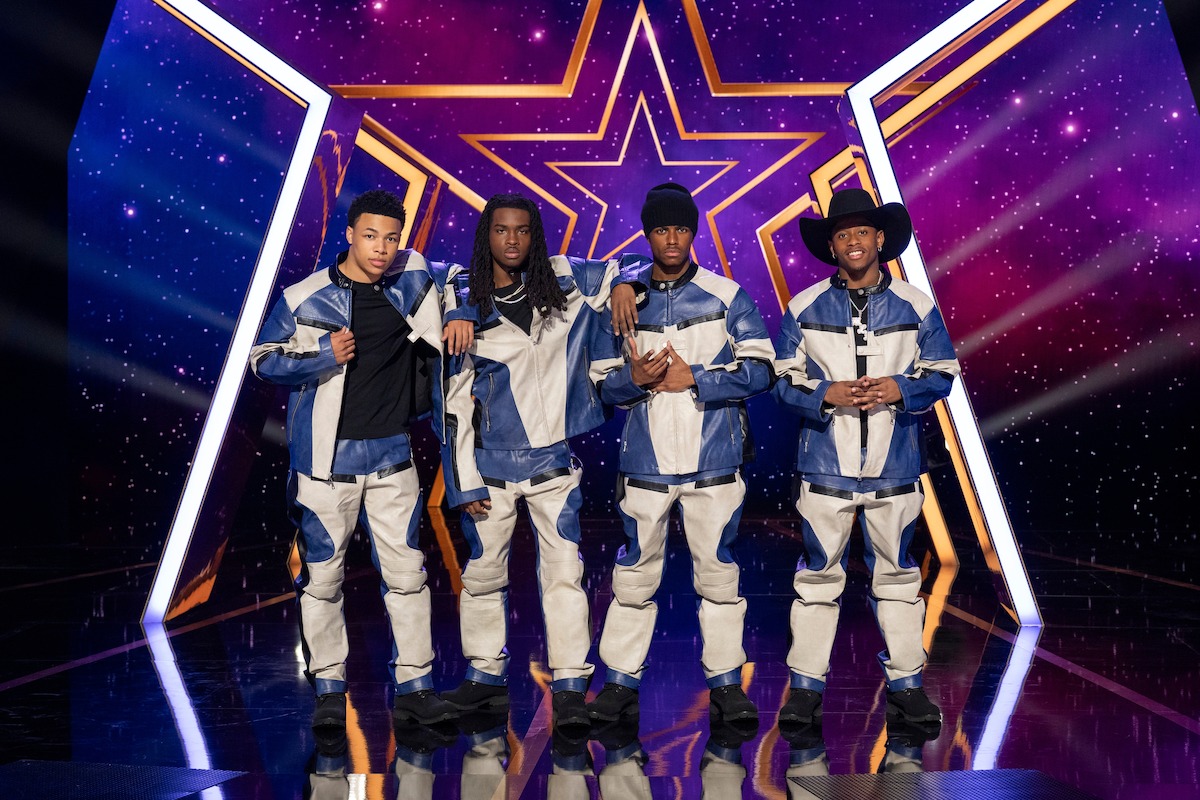 2BYG in matching blue and white outfits stand together on a shiny stage with a colorful starry background and a large star symbol behind them, suggesting a performance or talent show setting.