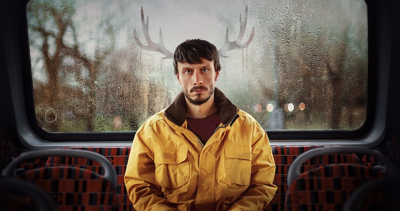 Richard Gadd as Donny Dunn sits in the back of a bus with reindeer antlers outside, behind his head in Season 1 of 'Baby Reindeer'