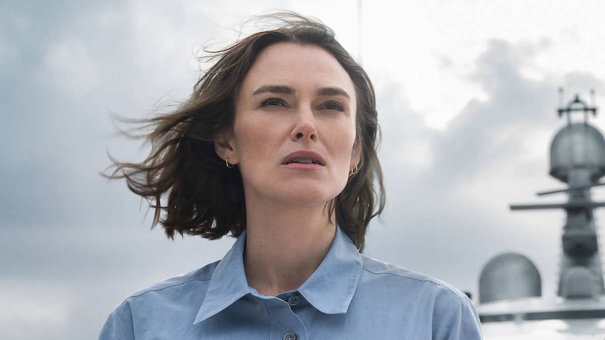 Kiera Knightley wearing a blue button down looks off into the distance while aboard the deck of a yacht.