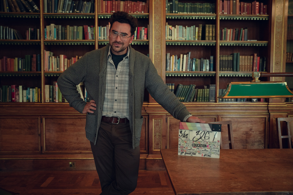 Dan Levy as Thomas Molloy stands by a desk with a clapboard.