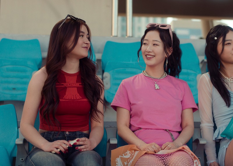 Anna Cathcart as Kitty Song Covey and Gia Kim as Yuri Han sit together on bleachers in Season 2 of 'XO, Kitty'