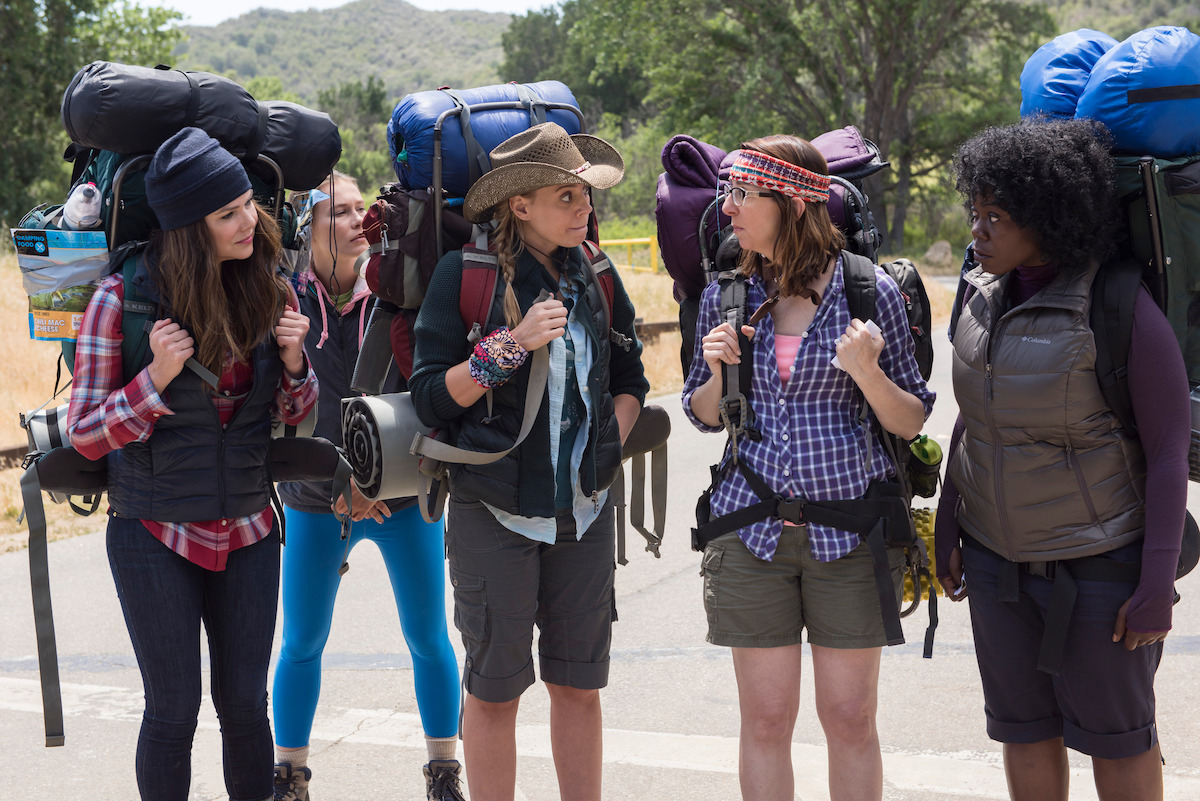 A group of backpackers stand and talk while wearing their backpacks