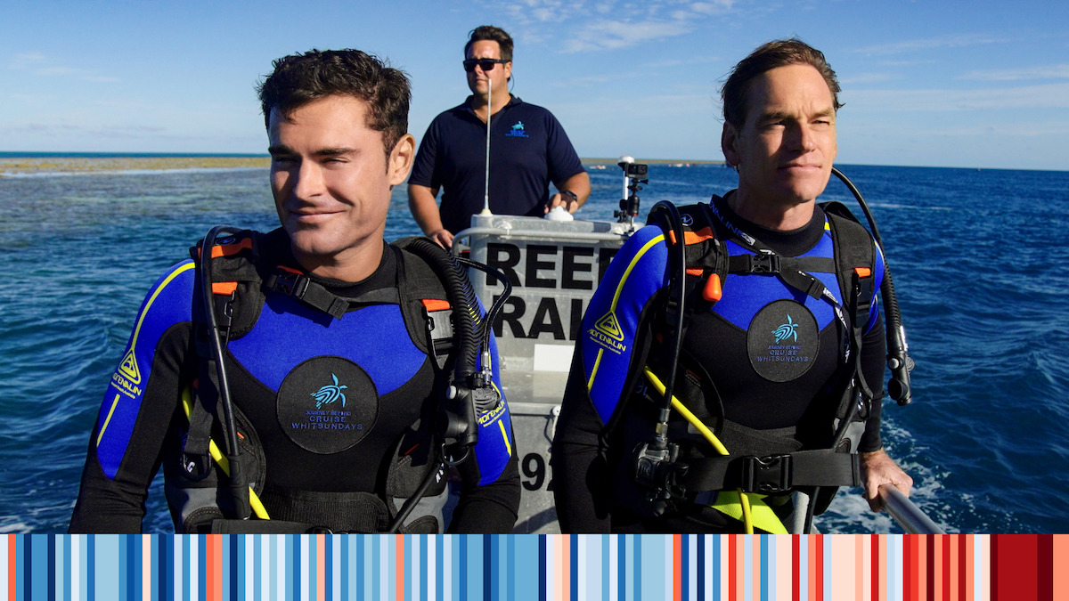 Zac Efron in scuba gear with two people on a boat at sea. 