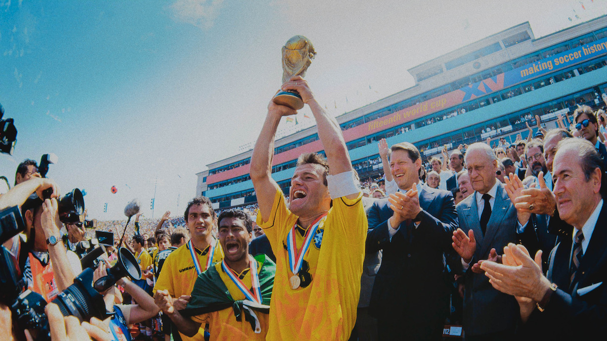 A player on Brazil’s 1994 World Cup team holding up the World Cup Trophy with his teammates and officials standing next to him.