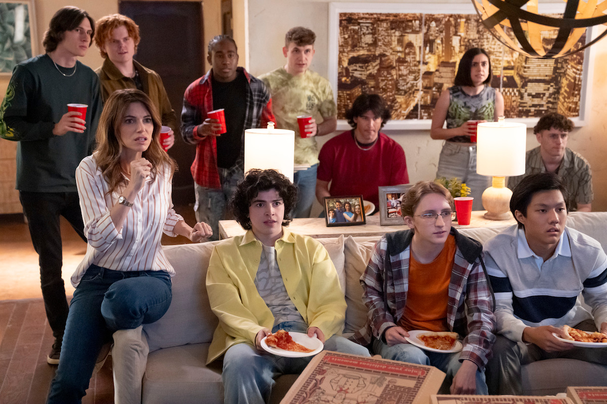 Courtney Henggeler as Amanda Larusso, Griffin Santopietro as Anthony LaRusso, Owen Morgan as Bert, and Nathaniel Oh as Nate watch TV with concerned expressions in Season 6 of ‘Cobra Kai.’