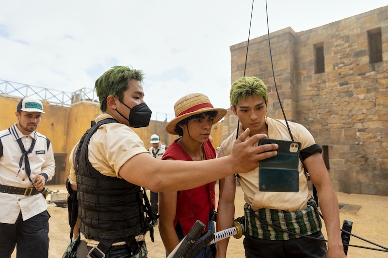 Stunt double/katana specialist Koji Kawamoto, Iñaki Godoy as Monkey D. Luffy, and Mackenyu as Roronoa Zoro look at a phone together in Season 1 of 'One Piece.'
