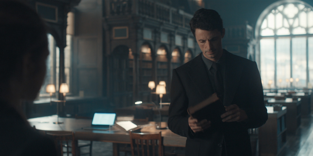 Matthew Goode as Matthew Clairmont stands holding an old book in the University of Oxford library in an image from ‘A Discovery of Witches.’