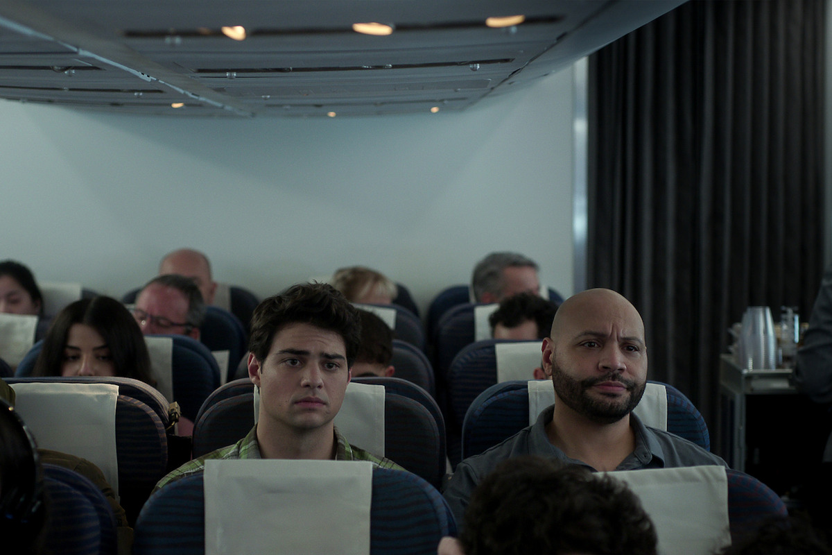 Noah Centineo sitting on an airplane looking bored.