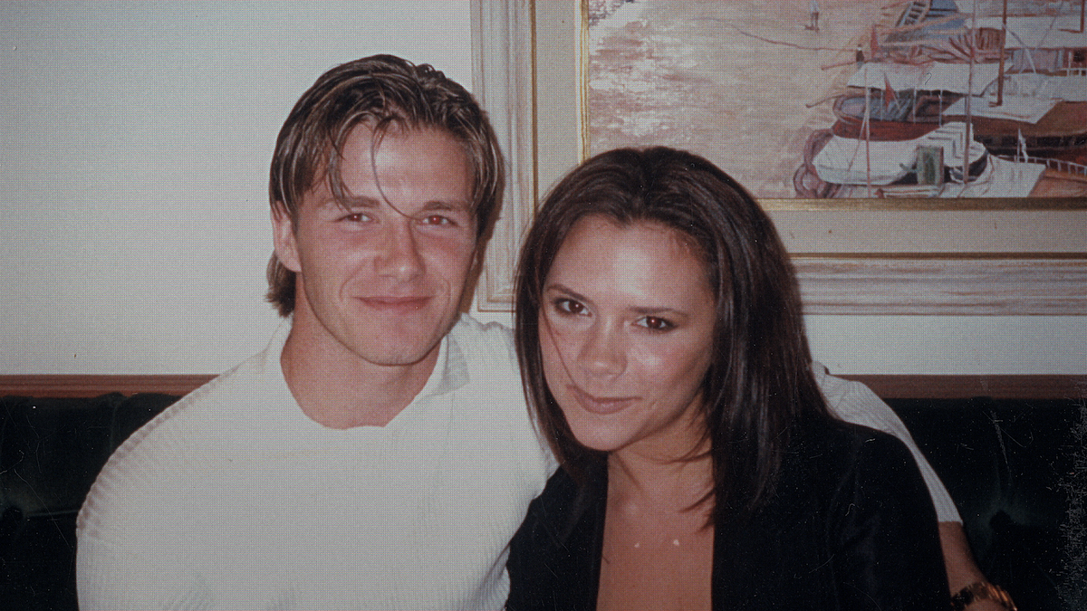 Candid photo of David Beckham with his arm around Victoria Beckham while they smile.