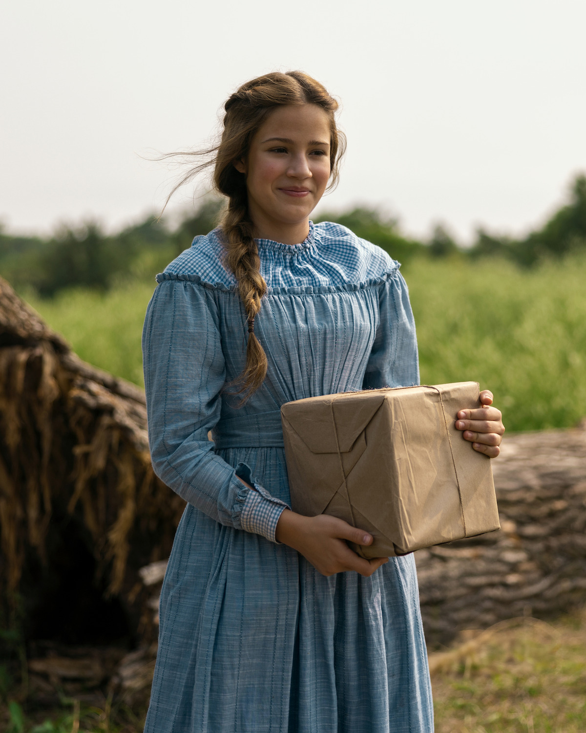 A girl holding a brown paper package smiles.