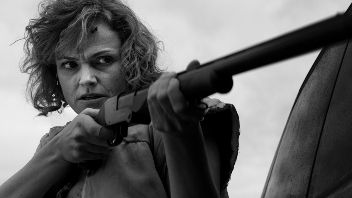 a black and white image of a woman holding a shotgun. 