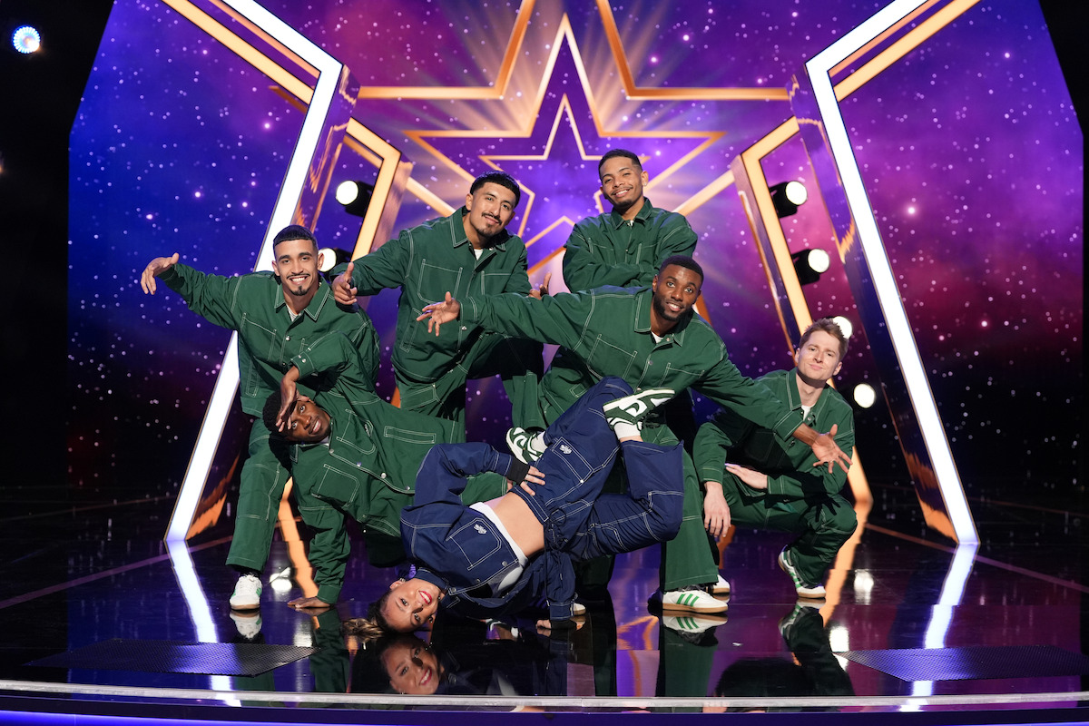 Rad Crew in green tracksuits pose on a stage with a starry purple background and a glowing star, while one dancer in blue performs a breakdance move on the floor in front.