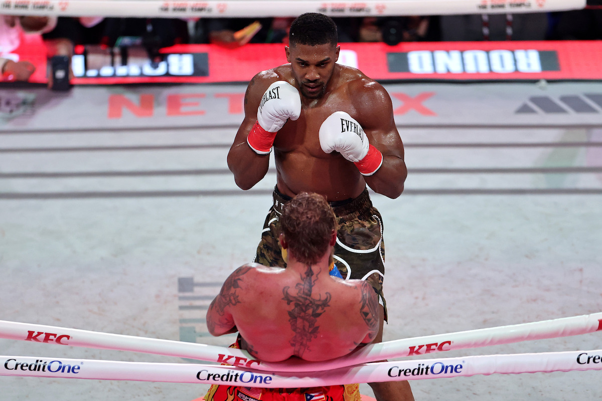 Jake Paul on the ropes as Anthony Joshua stands in front of him.
