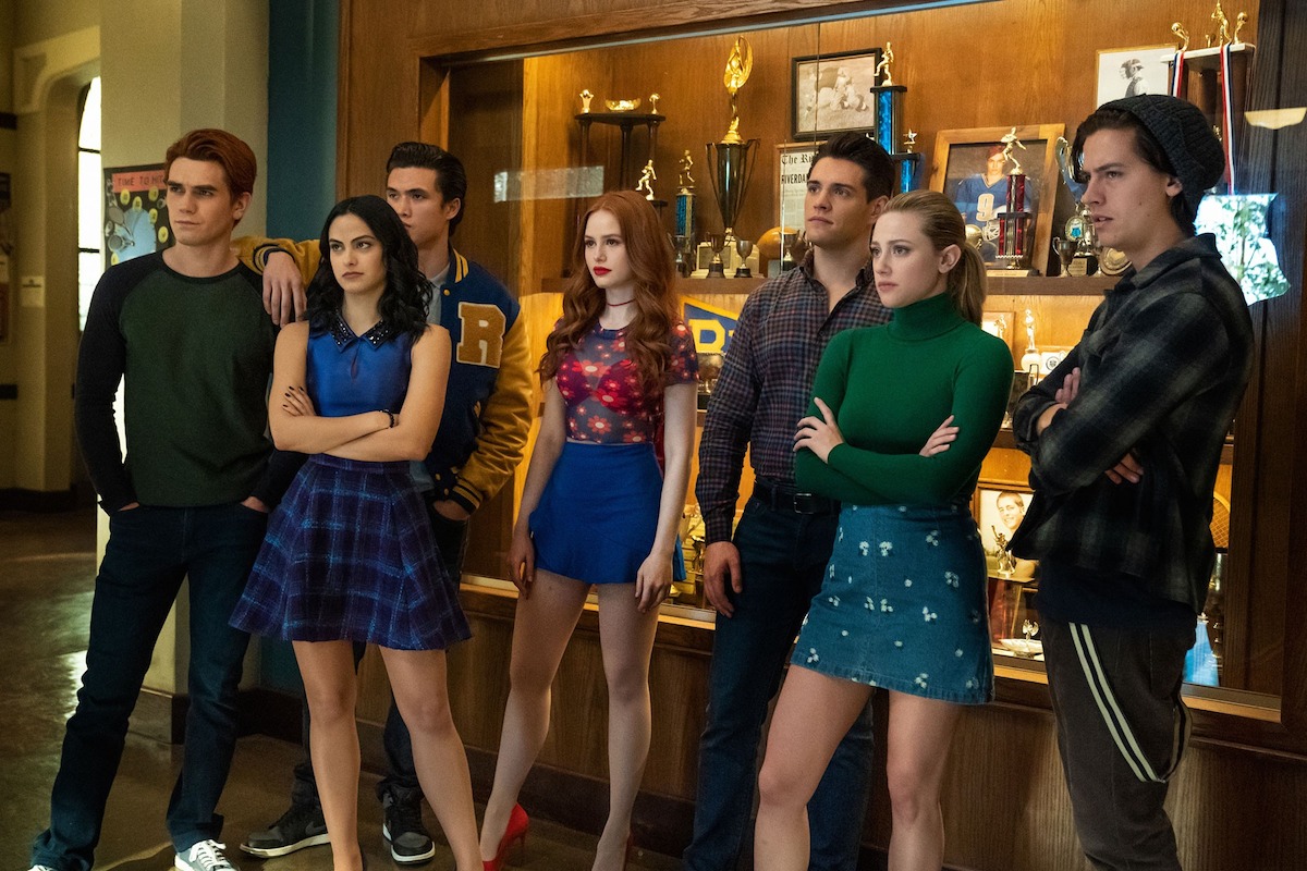 A group of teens stand by a trophy case at a high school.