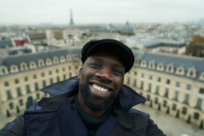 Omar Sy as Assane Diop smiles with the city of Paris in the background in Season 3 of 'Lupin.'