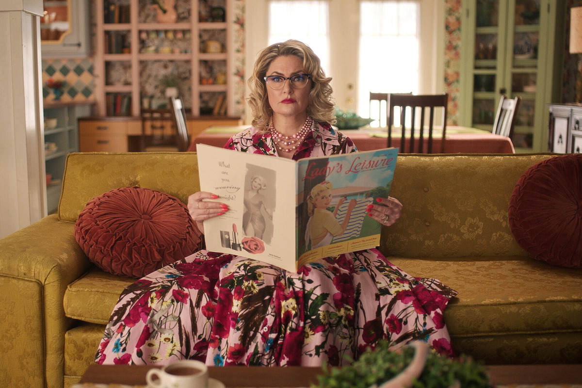 Mӓdchen Amick as Alice Cooper sits on a couch with a magazine in Season 7 of ‘Riverdale.’